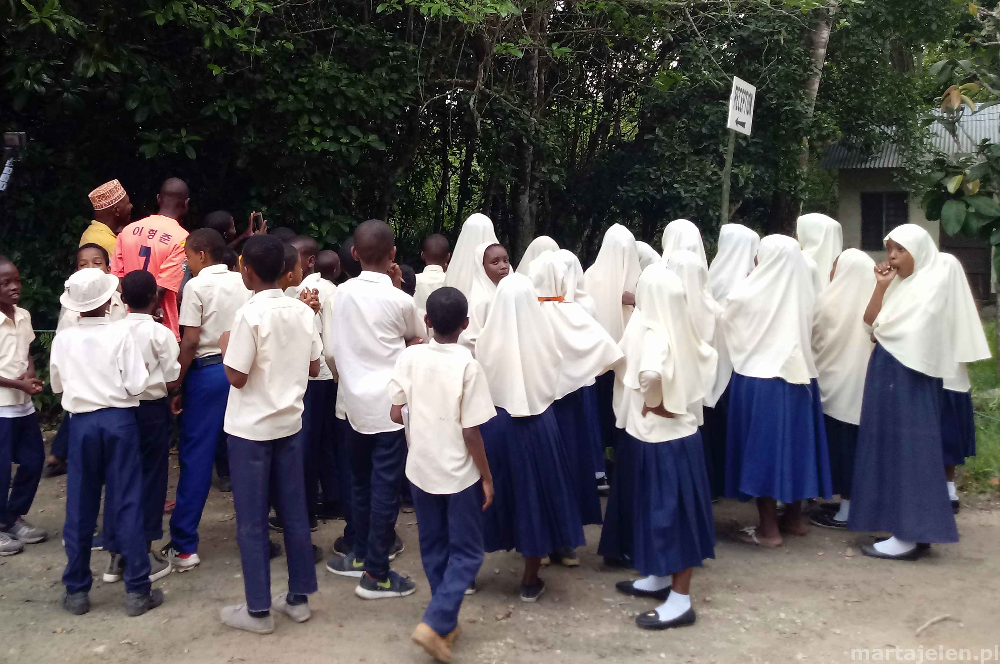 Tłum dzieci w mundurkach szkolnych słucha nauczyciela w Jozani
